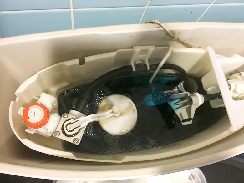 トイレのタンクのふたを開けて中を真上から見た写真。水がたまっており、左にレバーとつながる白い腕、中央に丸いゴム栓、右に水を入れる部品が見える
