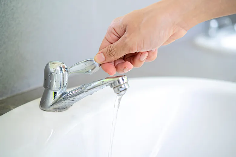 洗面台の蛇口を手でひねり、水が出ているところ