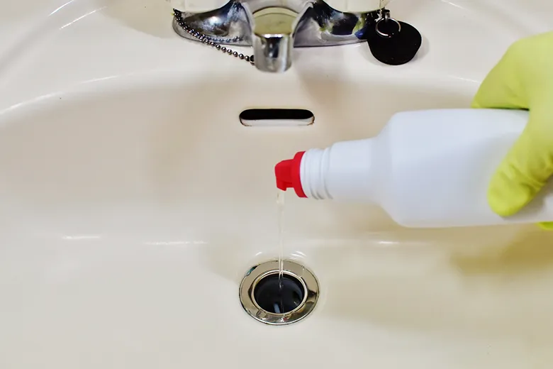 洗面ボウルの排水口に洗剤を注いでいるところ。ボウルの上にはオーバーフローの穴が見えている